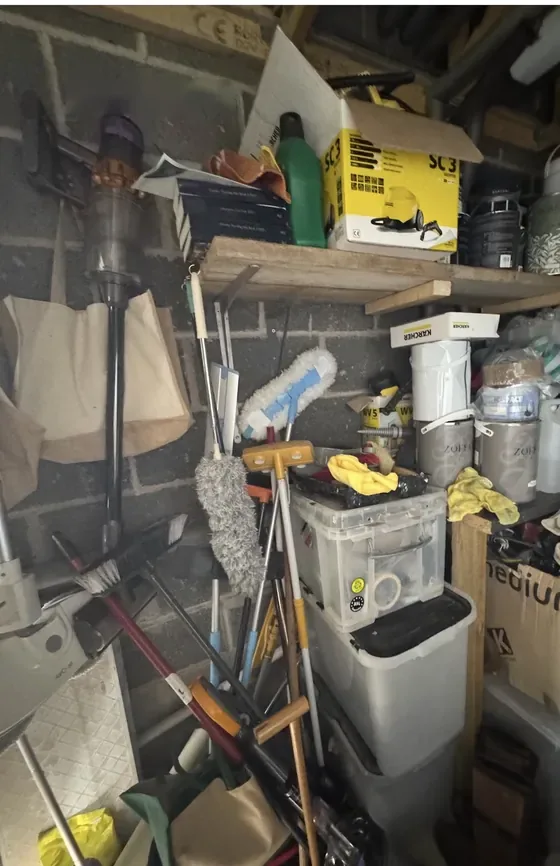 A garage corner before: shelves and floor stacked with tools, boxes, paint tins and cleaning gear