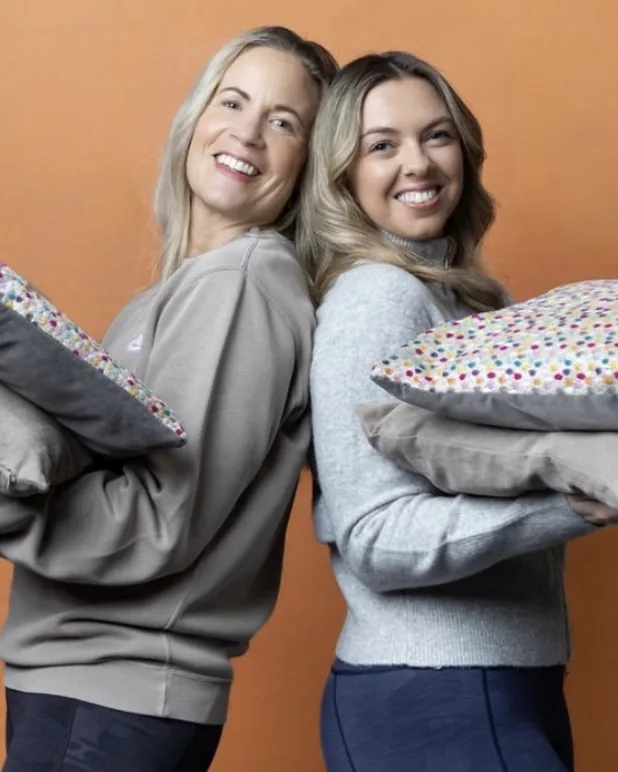 Jane and Alicia from Life Laundry UK, back to back, holding cushions and laughing
